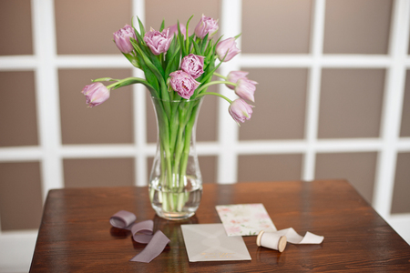 Lavender purple flowers in a golden vase on a wooden table in an elegant interior with greeting cards and a velvet box with decoration.の写真素材