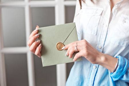 Close-up woman with slim body holding in hands the invitation card gray-green color square shape envelope card.の写真素材