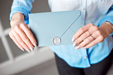 Close-up of a young girl holding a blue rectangular gift envelope with invitations, goods and services card.の写真素材