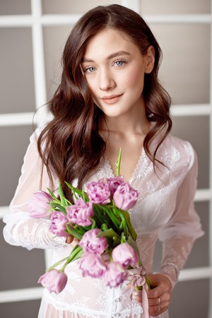 Young beautiful brunette girl holding spring bouquet of tulips in her hands.の写真素材