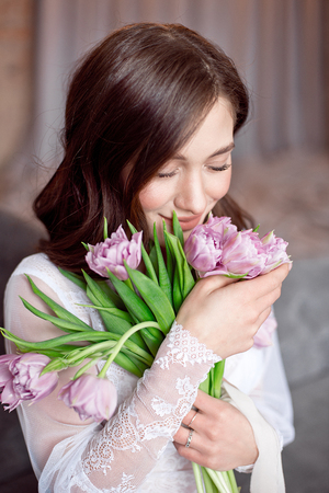 Young beautiful brunette girl holding spring bouquet of tulips in her hands.の写真素材
