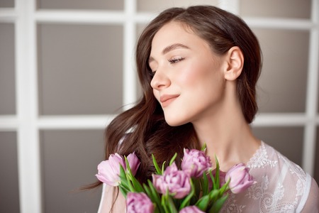 Young beautiful brunette girl holding spring bouquet of tulips in her hands.の写真素材