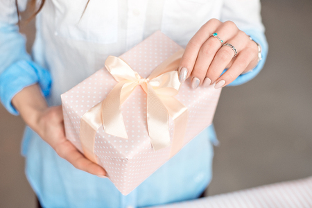 Close-up shot of female hands holding a small gift wrapped with pink ribbon. Small gift in the hands of a woman indoorの写真素材