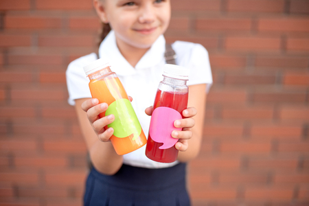 A girl holds in her hands healthy carrot juice to drink . Close-up of a orange glass bottle. Trend juice, raw, organic and cold-pressed.の写真素材