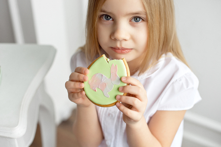 Close-up beautiful child is eating gingerbread eggs. Happy family preparing for Easterの写真素材