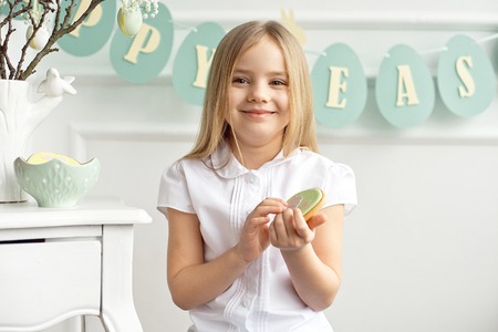 A cute toddler girl in a white shirt is eating with Easter eggs on Easter dayの写真素材