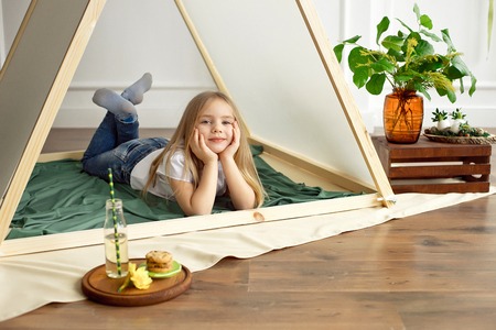 Cute happy little girl playing with toys and dreaming in teepee and bed.