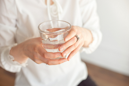 Female hands holding a clear glass of water.A glass of clean mineral water in hands, healthy drink.の写真素材