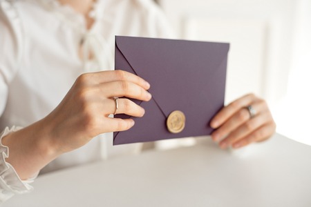Close-up woman with slim body holding in hands the invitation card purple color square shape...