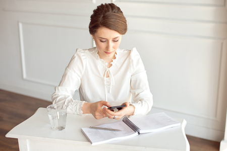 Portrait of a beautiful smiling young brunette businesswoman in a white shirt sitting on a bright modern workstation working with papers .の写真素材