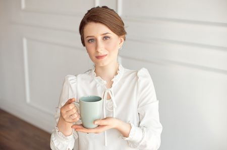 Attractive young woman in casual clothes is holding a cup, looking away and smiling, on white background.の写真素材