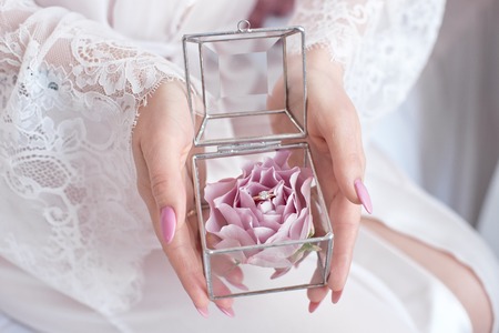 Close-up girl in a white dress holding a glass box, which are wedding rings.