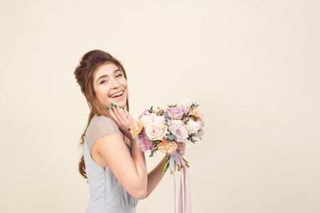 Elegant girl with a haircut in a soft blue dress and make-up is holding a bouquet of a stylish bouquet of flowersの写真素材
