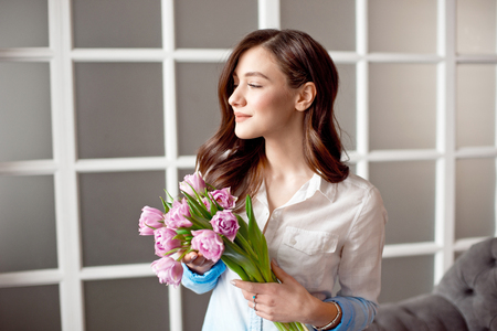 Young beautiful brunette girl holding a spring bouquet of tulips in her hands. Lifestyle.の写真素材