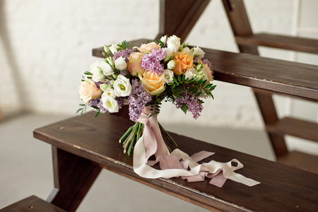 Wedding bouquet of pink roses with a lilac on a blurred background on a wooden staircase.の写真素材