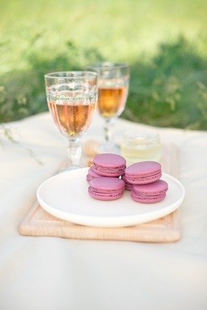 Light pink and fuchsia pink french macaroons or macaroons with glass goblets of pink wine in a round white plate on a beige tablecloth background with copy space.の写真素材