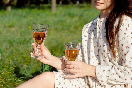 Cropped shot of a girl, in a summer dress, sitting with a glass of wine at a picnic while enjoying a picnic outdoors with wine on a summer day.の写真素材