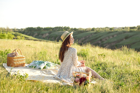 Happy Woman Life Style, beautiful relaxed girl in a straw hat on the nature picnic basket flowers in the rays of the soft sunset sun, a picnic - campingの写真素材