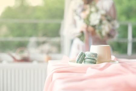 Young beautiful caucasian bride enjoying breakfast from french macaroon and coffee on a wooden table...