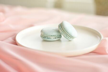 Blue macaroni or macaroon cakes with pink textile flowers on a white ceramic plate on a gray wooden...