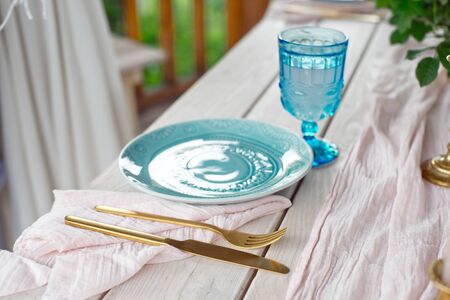 Table for guests, decorated with candles, served with cutlery and crockery and covered with a tablecloth blue plate and golden fork and knife on pink gauze napkin.の写真素材