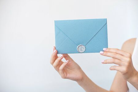 Close-up photo of female hands holding a silver blue or pink invitation envelope with a wax seal, a gift certificate, a postcard, a wedding invitation card.の写真素材
