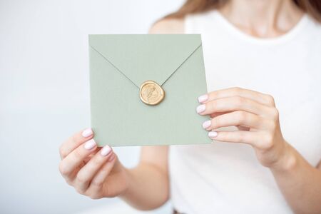 Close-up photo of female hands holding a silver blue or pink invitation envelope with a wax seal, a gift certificate, a postcard, a wedding invitation card.の写真素材