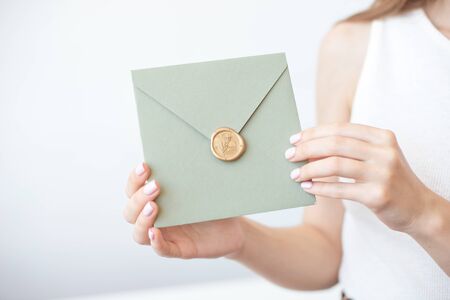 Close-up photo of female hands holding a silver blue or pink invitation envelope with a wax seal, a gift certificate, a postcard, a wedding invitation card.の写真素材