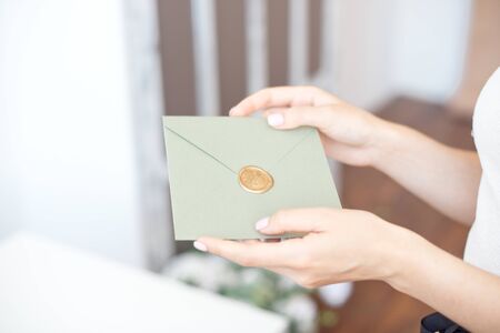 Close-up photo of female hands holding a silver blue or pink invitation envelope with a wax seal, a gift certificate, a postcard, a wedding invitation card.の写真素材