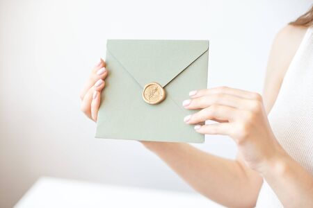 Close-up photo of female hands holding a silver blue or pink invitation envelope with a wax seal, a gift certificate, a postcard, a wedding invitation card.の写真素材