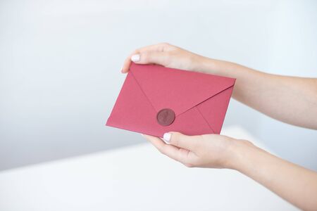 Close-up photo of female hands holding a silver invitation envelope with a wax seal, a gift certificate, a postcard, a wedding invitation cardの写真素材