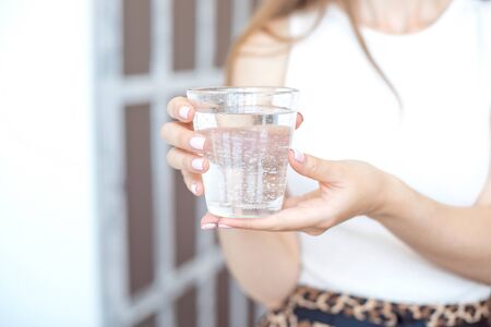 Close-up girl hands in the office stands in the sunlight holding a glass of clean water in between workの写真素材