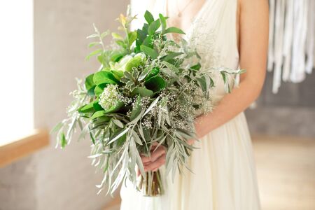 Slightly disheveled fresh and airy bridal bouquet with a grinn ball, brunia, eringum, eustoma, asparagus and eucalyptus in the hands of the bride in a white boho style wedding dress.の写真素材