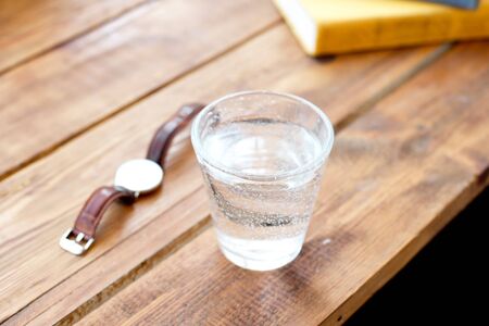 Clean glass of water on a wooden table while reading work books a clock to remind you to regularly take water a healthy lifestyle.の写真素材