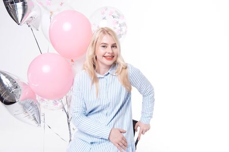Portrait of dress of a cheerful beautiful girl is standing near a bunch of colorful balloons and celebrating isolated over a blue background.の写真素材