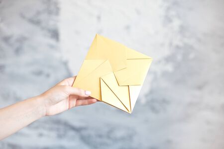 Female hand gives gold envelope square shape wedding invitation greeting card on gray background.