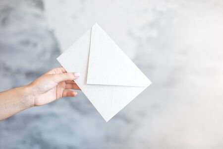 Female hand gives white envelope a wedding invitation on a gray backgroundの写真素材