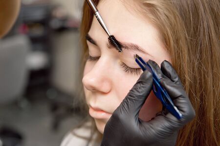Beautiful woman drawing a shape of eyebrows using cosmetic brush. Make up artist applying make up to a model.の写真素材
