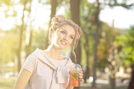 Young beautiful girl drinking fresh juice from plastic takeaway food cups after a walk outdoors....