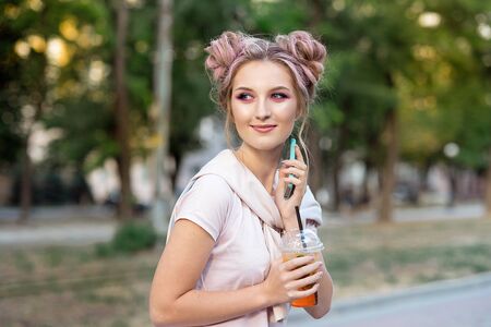 Happy cheerful young blonde with pink hair, walks against the backdrop of the city, calls on a mobile phone to his friends. Blonde student is resting on the street after college to meet friendsの写真素材