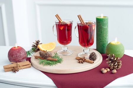 Two glasses of mulled wine with cinnamon sticks, a dry slice of oranges and cones, star anise on a white tableの写真素材