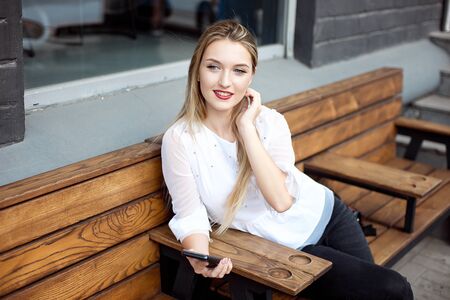 Beautiful pretty young businesswoman in cafe using cellphone and drinking coffee smiling.の写真素材