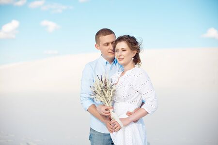 Young man and woman hugging on a background of white sand, dunes. Love story in the voidの写真素材