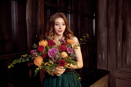 Halloween party girl. Happy Halloween beautiful girl in a black top and a full skirt in her hands holds a bouquet with autumn flowersの写真素材