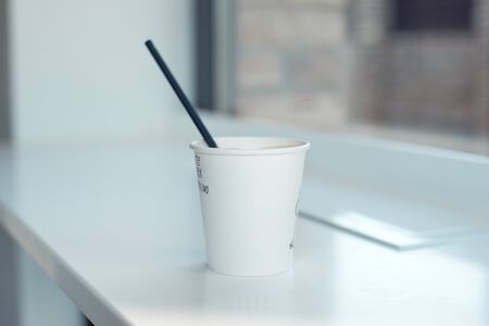 One simple takeaway paper cups on a white wooden table with a black paper tube.