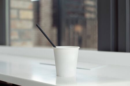 One simple takeaway paper cups on a white wooden table with a black paper tube.の写真素材