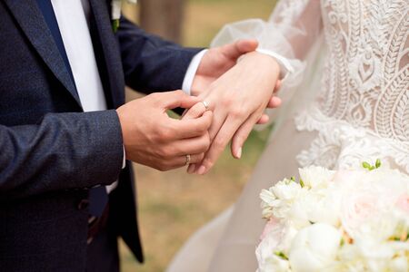 Groom wears bride a wedding ring Bride hand holds a beautiful wedding bouquet.の写真素材