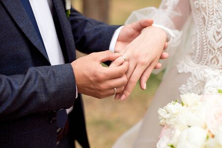 Groom wears bride a wedding ring Bride hand holds a beautiful wedding bouquetの写真素材