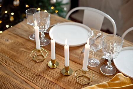 Table is served for a Christmas dinner in the living room, close-up view, table setting with a golden tablecloth, white plates, forks, knives, glasses for wine, candles in gold candlesticks, Christmas decorationsの写真素材