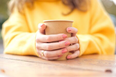 Girls hand holding a cup of kraft paper hot coffee in a cafe on the streetの写真素材